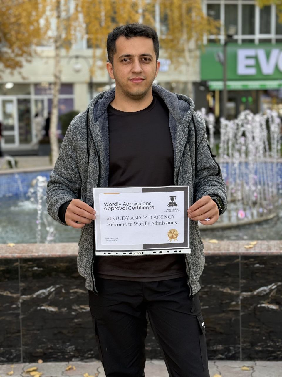 A Wordly Admissions student holding his approval certificate in front of a city fountain